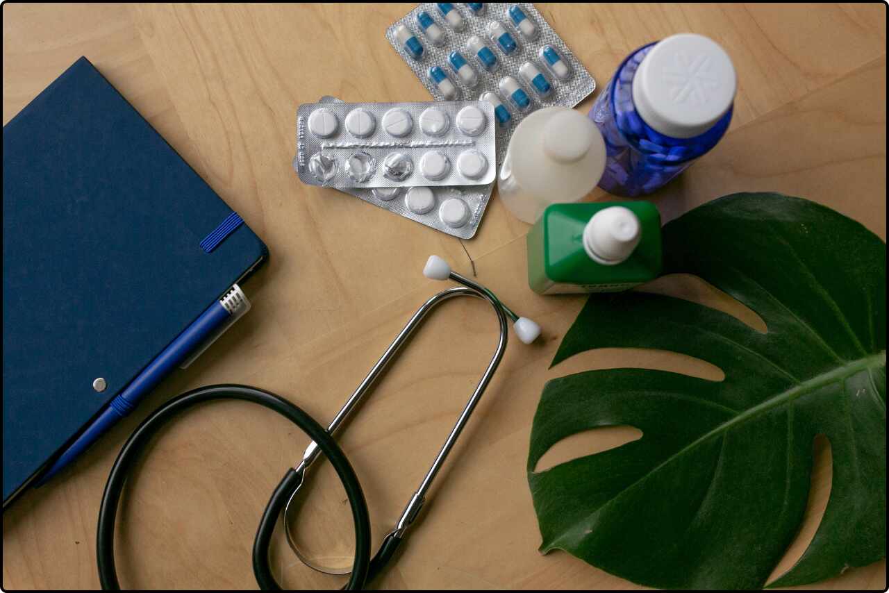 Flatlay shot of green medicine bottles and doctor's equipment on a wooden surface.